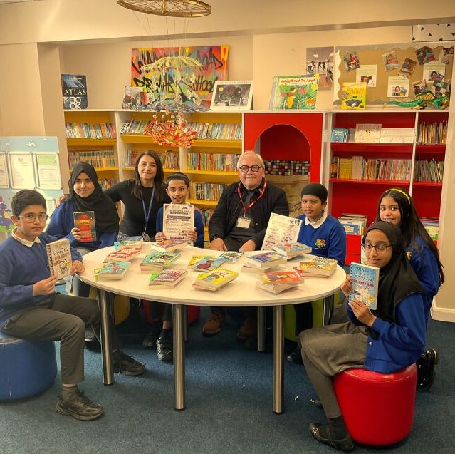 Trustee Graham sitting at a table alongside school pupils with books